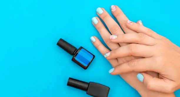 Woman's hands with beautiful manicure and bottles of nail polish on blue background.