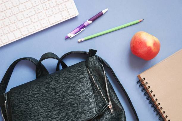 Computer keyboard, backpack, purple pen, green pencil, red apple and paper notebook. Back to school concept photography. Table top view