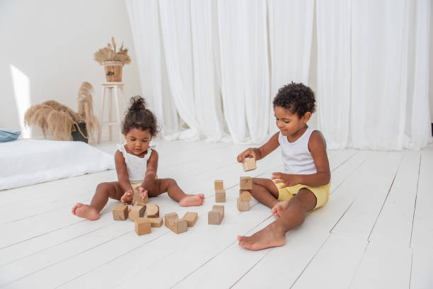 hermano pequeño y hermana afroamericanos negros juegan casas con ladrillos ecológicos de madera - cube baby child block fotografías e imágenes de stock