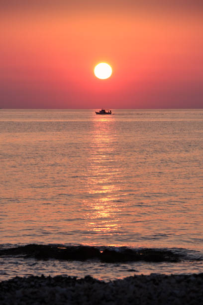 Fishing boat silhouetted on the ocean at sunrise, Marzamemi, Sicily, Italy