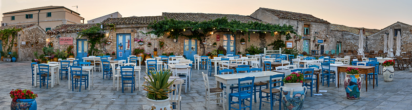 Tables and chairs setup in traditional Italian restaurants in the main square of the historic village Marzamemi, Syracuse, Sicily during a sunny day.