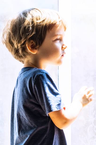 istock Pensive little boy looking out through a window 1268903190