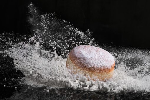 Berliner donut with jam stuffed  falls into flour on black background.