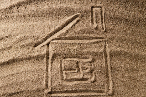 istock house symbol drawing on beach sand. hard shadow. property concept 1268917335