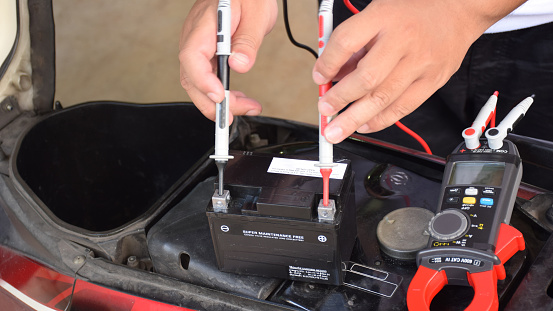 A mechanic is measuring the voltage of a motorcycle battery with clamp meter for maintenance. Thai text is mean 