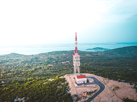 Photo of a 5G communication antennas and tower on top of a mountain summit. The sky is very clouded and it is a grey day.