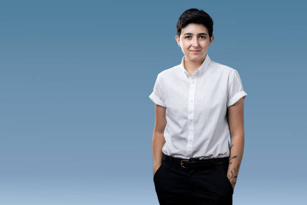 Spokesperson for the LGBTQI Community A gender non binary person with short hair stand in front of a blue background. They stand with hands in pant pockets. non binary gender stock pictures, royalty-free photos & images