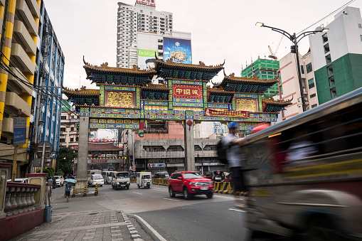A man rides standing on the back of a jeepney passing the Chinatown arch in Manila, Philippines (July 27, 2019)