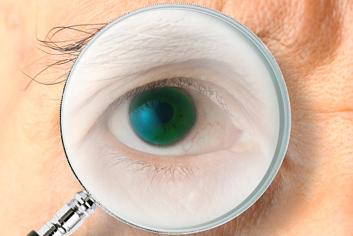 Extreme close-up of men’s blue eye looking through a magnifying glass.