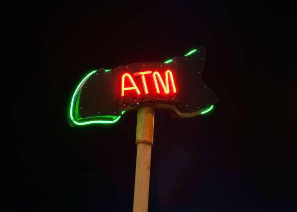 ATM neon sign on pole at night on black background.