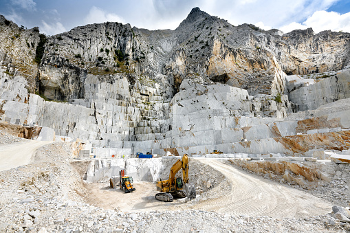 A large, yellow dump truck unloads gravel in gravel pit next to a small green lake, aerial view.