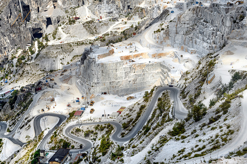 Panorama view of Carrara marble quarries in a steep mountain valley showing open cast mining and a winding road in Tuscany Italy