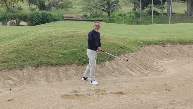 asian chinese senior man golfer fail hitting his golf ball in a sand trap with his iron club