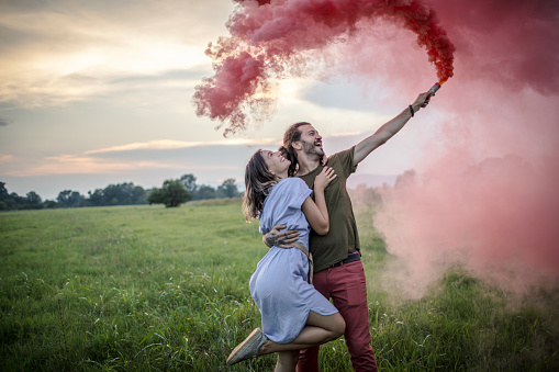 Playful young couple having fun with red smoke bomb and celebrate their love