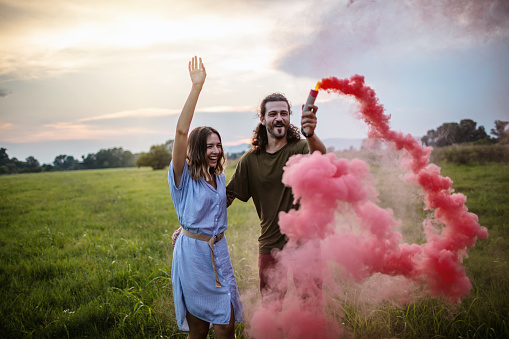 Playful young couple having fun with red smoke bomb and celebrate their love