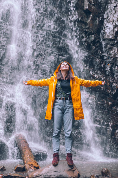 istock woman in yellow raincoat at autumn waterfall 1268993774