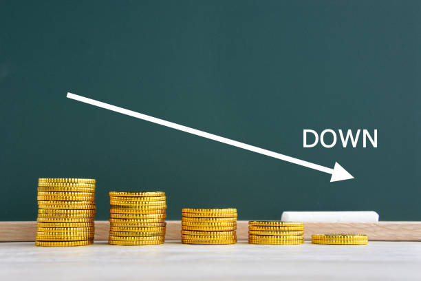 istock Gradually Piled coins and downward arrow on black board 1269019388