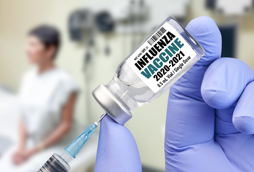 Nurse holding Influenza Flu Vaccine 2020-2021  bottle for injection with syringe to give shot to woman in doctor’s office.