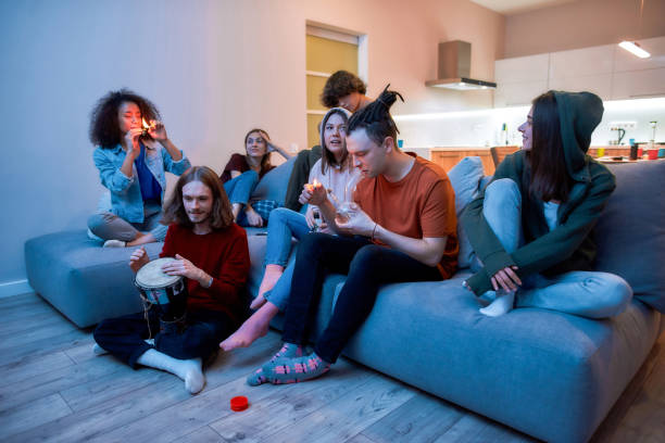 joven iluminando marihuana en el bong de cristal y fumando, relajándose con amigos en el sofá en casa, jóvenes fumando hierba juntos - sofa music teenager friendship fotografías e imágenes de stock