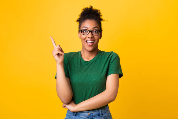 Excited teenager has great idea and points up I Got It. Overjoyed african lady in eyeglasses having idea, pointing up and looking at camera over green wall black nerd stock pictures, royalty-free photos & images