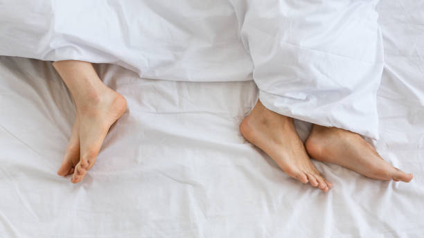 problemi nelle relazioni familiari. piedi di uomo e donna in letto bianco a distanza - temi legati alla sessualità foto e immagini stock