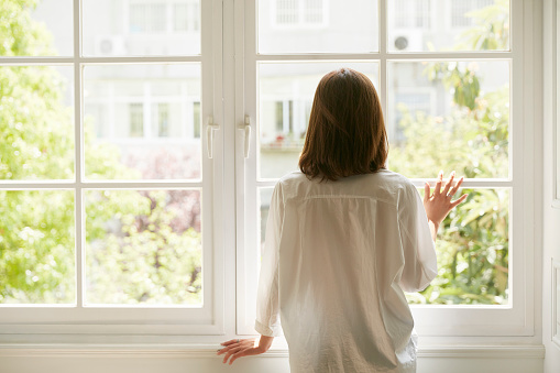 rear view of a young asian woman looking out of window at home