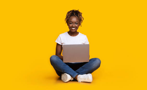 istock Black girl sitting on floor, using laptop, yellow background 1269034666