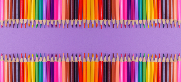 A close up row of brightly colored pencils on a purple background.  Flat lay with copy space.