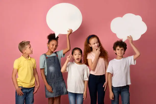 Photo of Cute multinational schoolchildren with empty speech bubbles over pink background, space for design