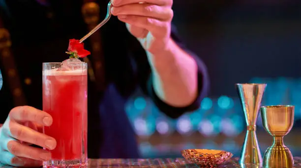 Photo of Great flavour. Close up of bartender hand decorating cocktail in glass with rose flower while making alcoholic drink at the bar counter in the night club