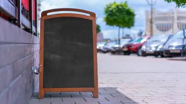 empty black chalkboard with mock-up in wooden frame stands on sidewalk food cafe menu concept front view