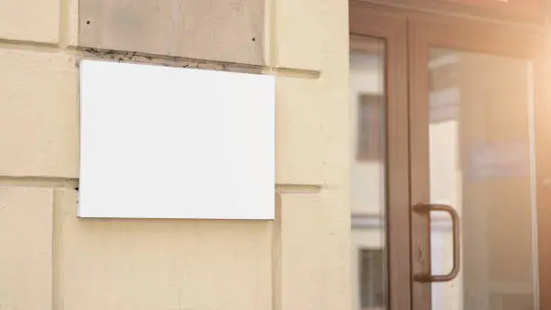 blank white sign board on concrete wall near closed door of store or office building outside