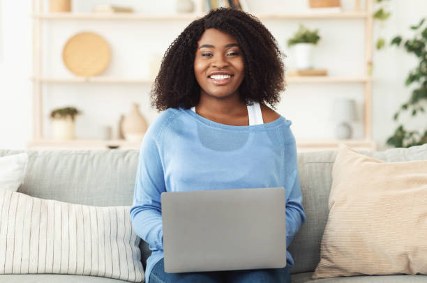 istock Black woman sitting on couch with pc looking at camera 1269046009