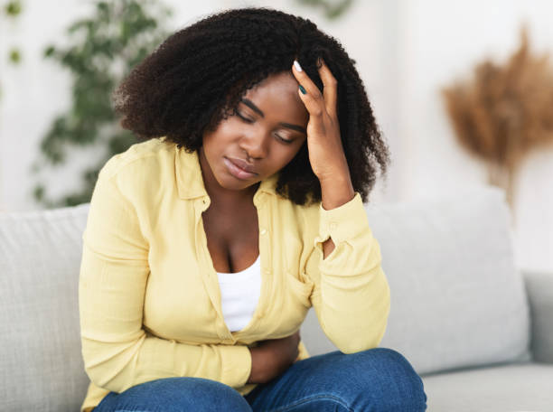 Tired african american woman suffering from pain Sad black woman suffering from PMS and menstruation pain. Having stomach ache, abdominal pain and headache endometriosis black women stock pictures, royalty-free photos & images