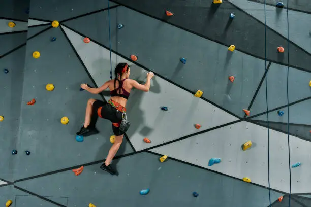 Photo of Woman in safety equipment and harness training on the artificial climbing wall indoors