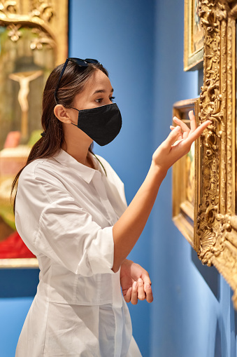 girl visitor wearing an antivirus mask standing near pictures in museum