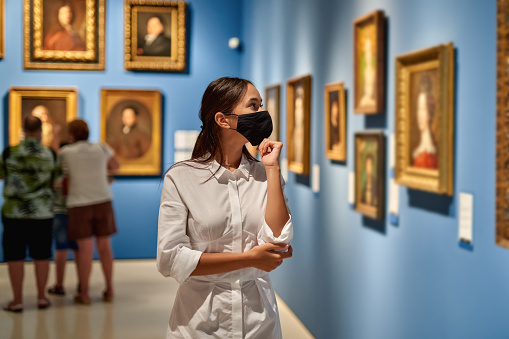 Mujer visitante que lleva una máscara antivirus en el museo histórico mirando imágenes. photo