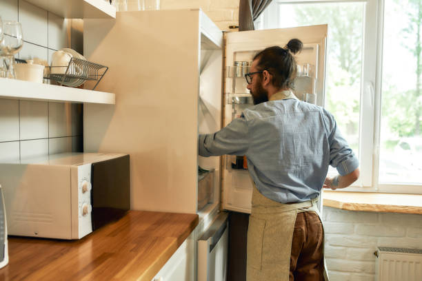 istock Young man, professional cook in apron taking ingredients out of the fridge while getting ready to prepare a meal, standing in the kitchen. Cooking at home concept 1269052403