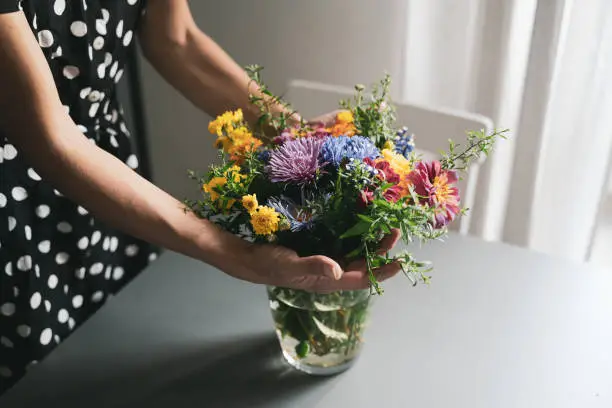 Photo of woman arranging a bouquet of flowers in a glass vase