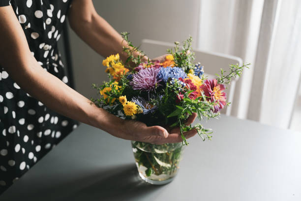 woman arranging a bouquet of flowers in a glass vase - flower arrangement flower bouquet arrangement imagens e fotografias de stock