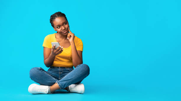 istock Thoughtful African American Girl Sitting Using Cellphone, Blue Background 1269063623