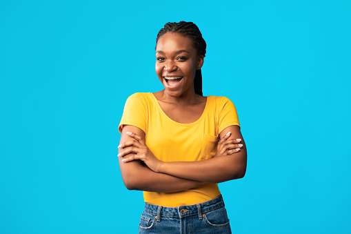 Cheerful African Millennial Girl Posing Crossing Hands Smiling To Camera Over Blue Studio Background.