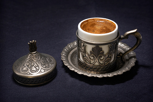 View of Turkish coffee and traditional cup. Turkish coffee is a style of coffee prepared using very finely ground coffee beans without filtering. Despite the name, the style originated in Yemen.