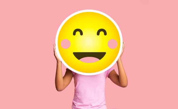 Black girl hiding face behind happy shy emoji emoticon on pink background Black girl hiding face behind happy shy emoji emoticon, standing over pink studio background with copy space blush emoji stock pictures, royalty-free photos & images