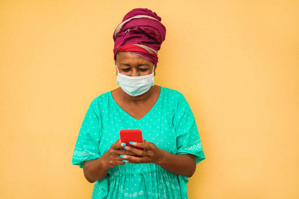 istock Senior african woman using mobile phone while wearing face protective mask for coronavirus prevention - Lifestyle, technology, ethnic and Covid 19 protections concept 1269081136