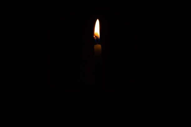 istock Close up single burning, bright white paraffin candle light on isolated dark black background. Red, orange, yellow candle fire flame smoke in party festival celebration at night. Copy space for text. 1269083167