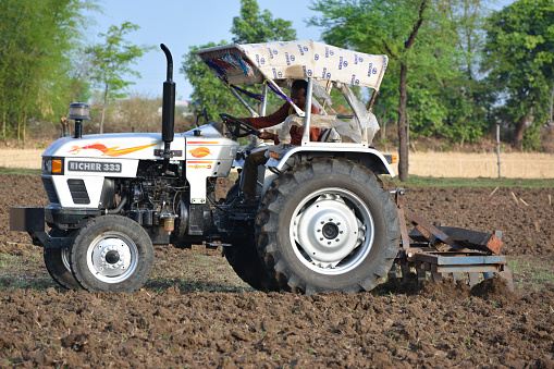 TIKAMGARH, MADHYA PRADESH, INDIA - JUNE 15, 2020: Indian farmer with tractor preparing land for sowing with harrow.