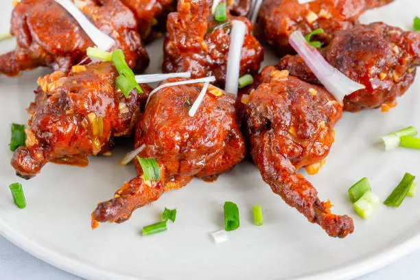 Popular Indo-Chinese Chicken Appetizer Made of Chicken Winglets on a White Plate Close-Up Photo