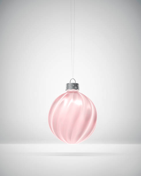 Pink toned glossy twisted ribbed Christmas ball hanging over white background. Diffused light. Christmas decoration, festive atmosphere concept.