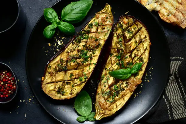 Grilled spicy eggplants on a black plate on a dark slate, stone or concrete background. Top view with copy space.